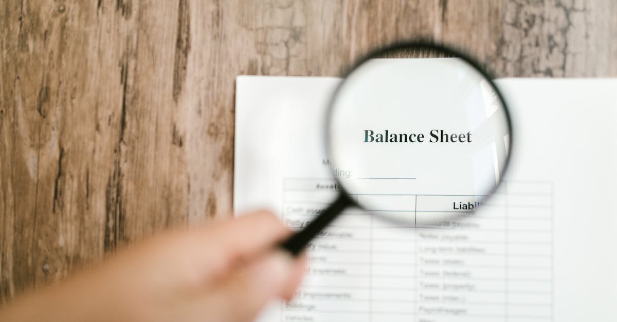 Close-up of a balance sheet document on wooden surface with a magnifying glass held by a hand.